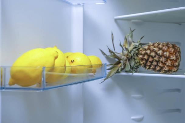 Open fridge full of fruits with many ripe lemons and pinapple. blue light.  - Foto, afbeelding