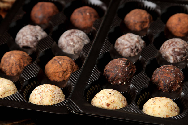 Chocolates variados. Bolas de doces de diferentes tipos de chocolate em uma caixa em uma mesa de madeira marrom
. - Foto, Imagem