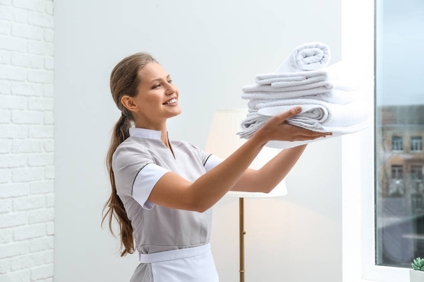 Beautiful female housekeeper with clean towels in room - Foto, immagini