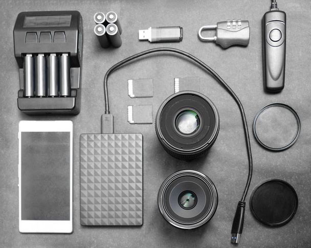 Workspace of photographer. Top view with black table, photo flas, lens, smartphone, remote control, compact disk and battery charger.  - Photo, image