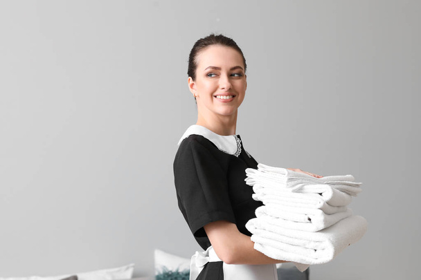 Prachtige vrouwelijke huishoudster met schone handdoeken in kamer - Foto, afbeelding