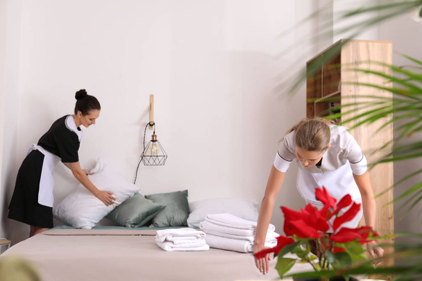 Prachtige vrouwelijke huishoudsters maken van bed op kamer - Foto, afbeelding