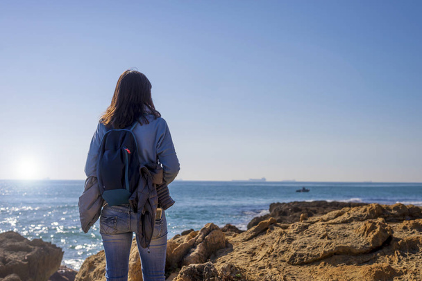 Pohled zezadu mladá žena nosí ležérní oblečení, stojící na pláži při pohledu daleko v jasný den - Fotografie, Obrázek