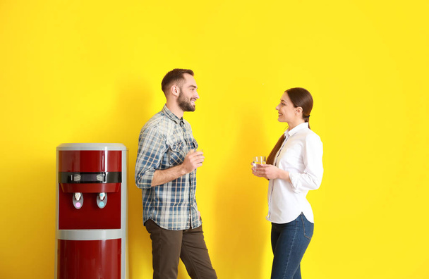 Man and woman drinking water from cooler against color background - Foto, immagini