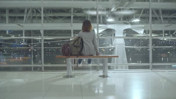 glückliche asiatische Frau, die sich auf einem Stuhl in der Terminalhalle umschaut, während sie am Abflugsteig des internationalen Flughafens auf ihren Flug wartet. Lifestyle-Frauen glücklich im Flughafenkonzept. - Filmmaterial, Video
