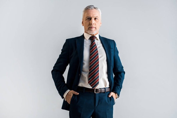 sérieux homme d'affaires mature debout avec les mains dans des poches isolées sur gris
  - Photo, image