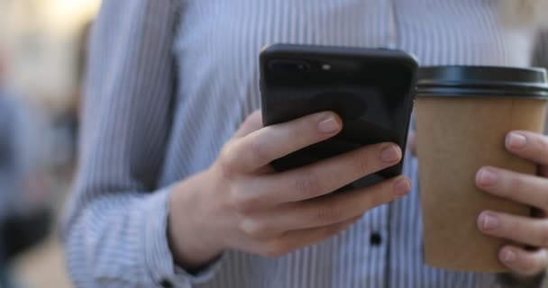 Jovem mulher de negócios em uma camisa segurando telefone celular e café em suas mãos e mensagens de texto, close-up vista
. - Filmagem, Vídeo