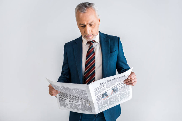 зрелый мужчина в костюме читает деловую газету, стоя изолированным на сером
  - Фото, изображение