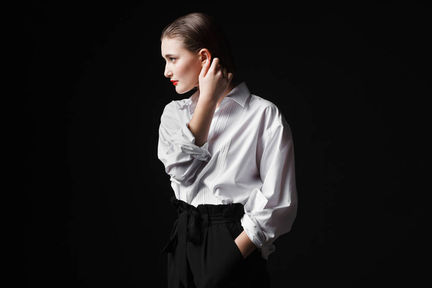 Portrait of an elegant young woman in a white shirt and black pants. Interesting studio light - 写真・画像
