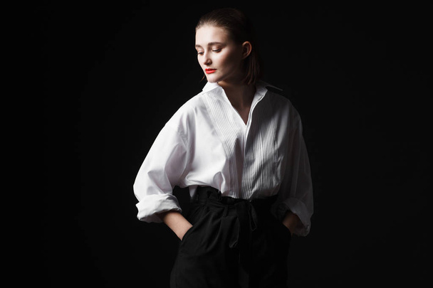 Portrait of an elegant young woman in a white shirt and black pants. Interesting studio light - Valokuva, kuva