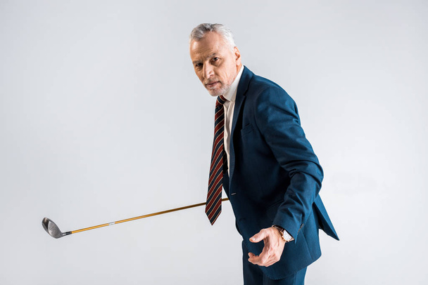 konzentrierte reifen Geschäftsmann hält Golfschläger, während spielen isoliert auf grau   - Foto, Bild