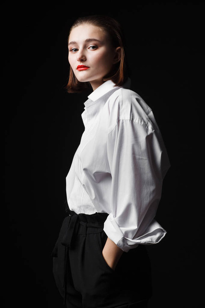 Portrait of an elegant young woman in a white shirt and black pants. Interesting studio light - Foto, afbeelding