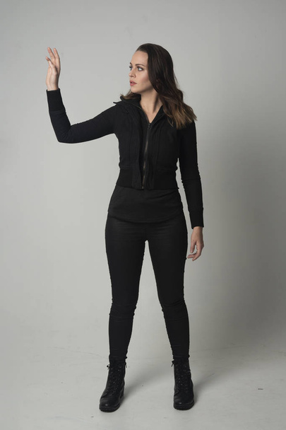 portrait complet d'une fille brune portant une veste et un pantalon noirs modernes, pose debout sur fond de studio gris
. - Photo, image