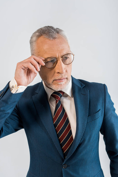зрілий бізнесмен торкається окулярів, стоячи ізольовано на сірому
 - Фото, зображення