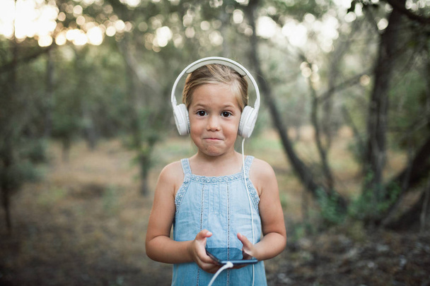 Μικρό κορίτσι ακούγοντας μουσική με τα ακουστικά της στο δάσος - Φωτογραφία, εικόνα