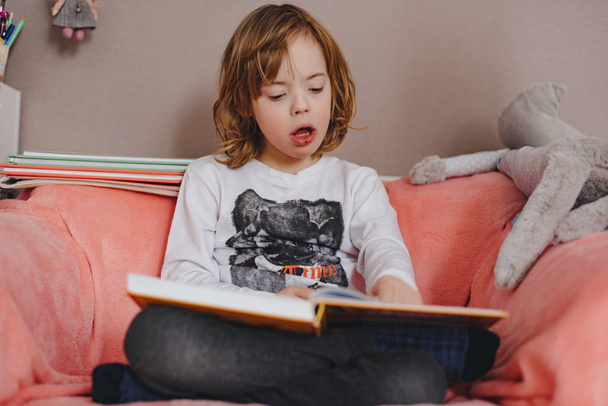 little boy reading book on sofa at home - Fotó, kép
