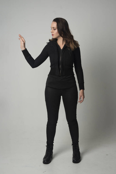 po celé délce portrét bruneta dívky nosí moderní černá bunda a kalhoty, stojící pozice na šedé studio pozadí. - Fotografie, Obrázek