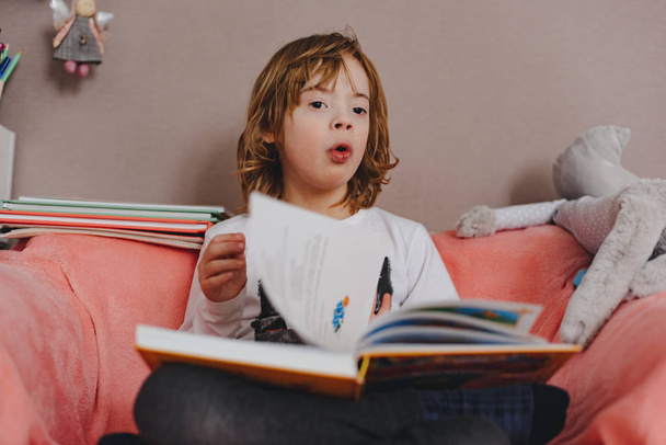 little boy reading book on sofa at home - Valokuva, kuva