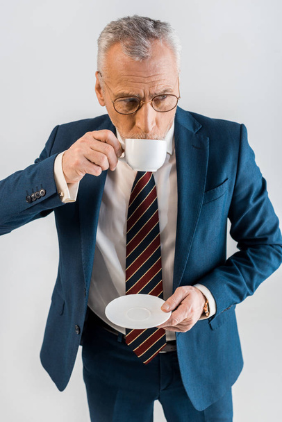 overhead view of mature businessman holding saucer and drinking coffee from cup isolated on grey - Zdjęcie, obraz
