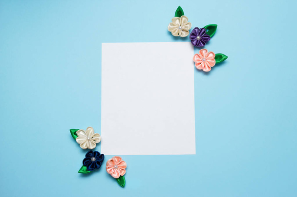 Paper blank with satin flowers and copy space on a blue background. Top view, flat lay. Spring concept - Photo, Image