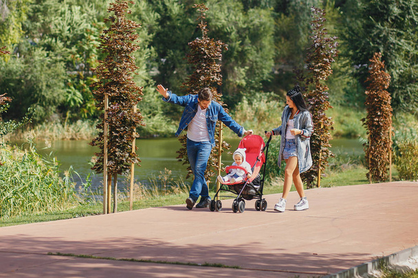 mamma e papà stanno passeggiando nel parco con la figlia in un passeggino, una bella giornata di sole, una bella famiglia
 - Foto, immagini