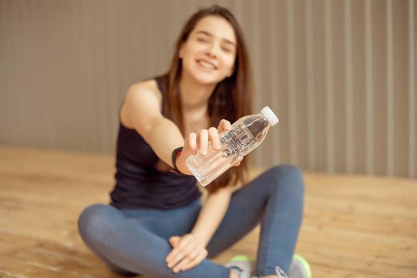 Female athlete takes a break with drinking water after a workout an athlete in sportswear holds a bottle of drinking water in the gym during a break. - Foto, Imagem