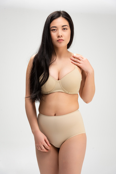 pretty overweight woman in underwear looking at camera isolated on grey, body positivity concept - Foto, Imagem