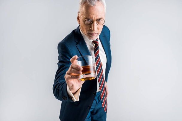 selective focus of mature businessman in formal wear holding glass with whiskey isolated on grey  - Фото, зображення