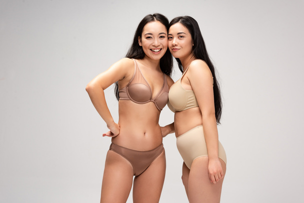 two happy multicultural girls in underwear hugging and looking at camera isolated on grey, body positivity concept - Φωτογραφία, εικόνα