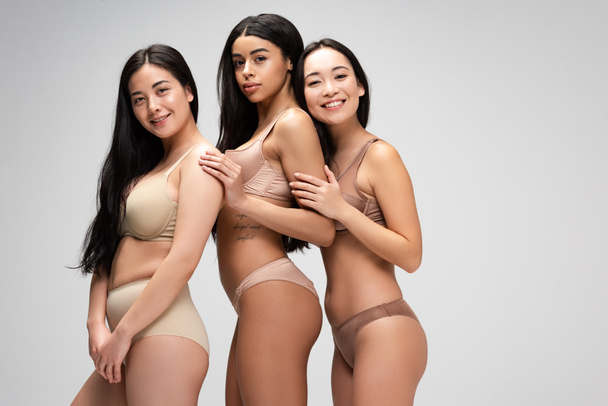 three beautiful multiethnic girls in lingerie looking at camera isolated on grey, body positivity concept - Photo, Image