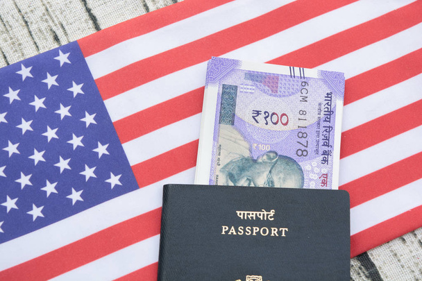 Close-up van Indiase paspoort met valuta op de vlag van Verenigde Staten of Amerika als achtergrond - Foto, afbeelding