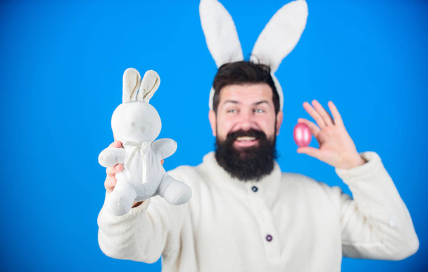 Spring symbols. Hipster with long rabbit ears holding egg laying hare. Celebration of spring time holiday. Bearded man with bunny toy and Easter egg. Easter bunny delivering colored eggs - Zdjęcie, obraz