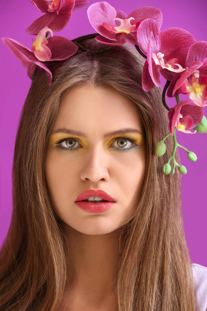 Όμορφη νεαρή γυναίκα με λαμπερό μακιγιάζ και λουλούδια στο χρώμα φόντου - Φωτογραφία, εικόνα