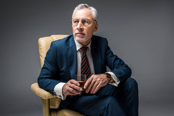středního věku podnikatel v obleku sedí v křesle a drží sklenici whisky Grey - Fotografie, Obrázek
