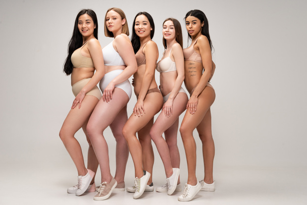 cinco hermosa mujer multiétnica en ropa interior y zapatillas de deporte posando en la cámara y sonriendo, concepto de positividad corporal
 - Foto, imagen