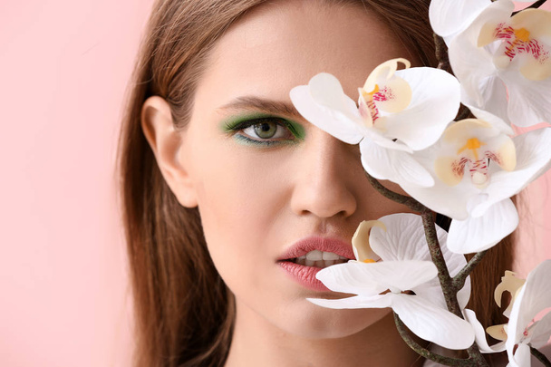 Gyönyörű fiatal nő, ragyogó smink és virág szín háttér - Fotó, kép