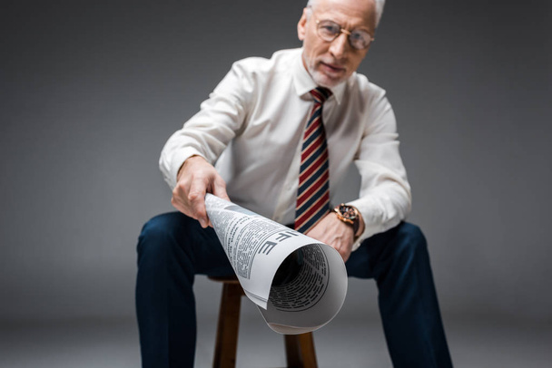 selective focus of newspaper in hand of mature businessman on grey  - Photo, Image