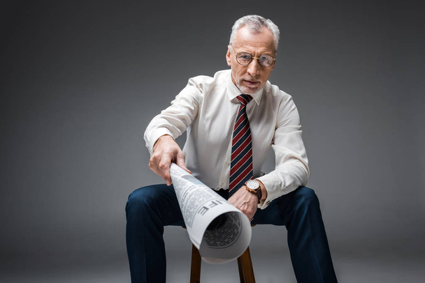 selective focus of mature businessman in glasses holding newspaper on grey  - Fotografie, Obrázek