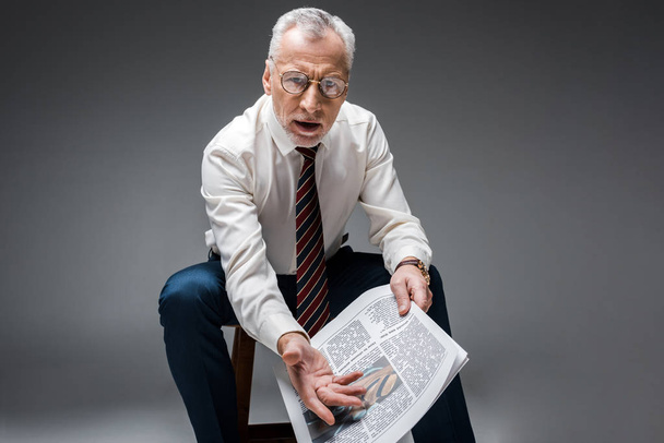 mature businessman gesturing while holding newspaper on grey  - Fotografie, Obrázek