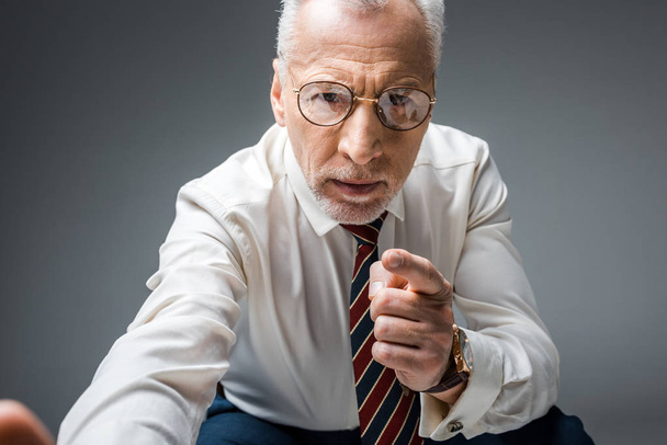 middle aged businessman in glasses pointing with finger while looking at camera on grey  - Foto, immagini