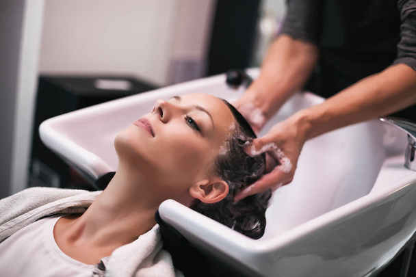 Mulher jovem recebendo novo penteado no salão de cabeleireiro profissional. Cabeleireira está massageando a cabeça
.  - Foto, Imagem