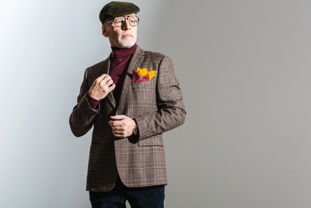 élégant homme d'âge moyen dans des lunettes et casquette debout sur gris
  - Photo, image