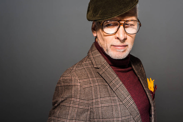 задумчивый и стильный зрелый мужчина в кепке и очках, стоящих на сером
 - Фото, изображение