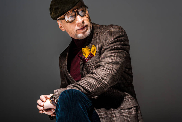 trendy en nadenkend volwassen man in cap en bril op grijs  - Foto, afbeelding