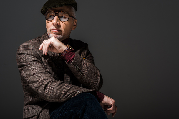 pensive mature man in glasses and cap thinking on grey - Foto, afbeelding