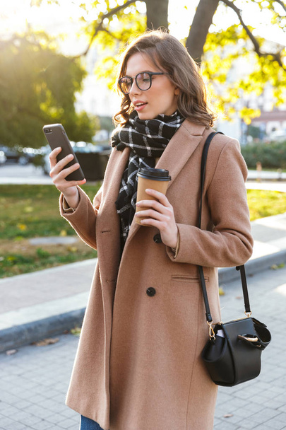 Щаслива молода жінка використовує мобільний телефон на відкритому повітрі, що йде вулицею
. - Фото, зображення