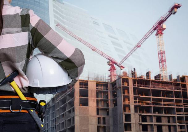 Eine Bauarbeiterin mit weißem Helm vor städtischem Hintergrund - Foto, Bild