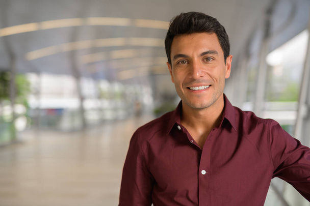 Gesicht eines glücklichen hispanischen Geschäftsmannes, der auf der Fußgängerbrücke lächelt - Foto, Bild