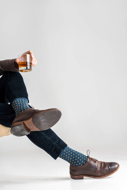 vista ritagliata di uomo maturo con gambe incrociate in possesso di un bicchiere di whisky su grigio
 - Foto, immagini