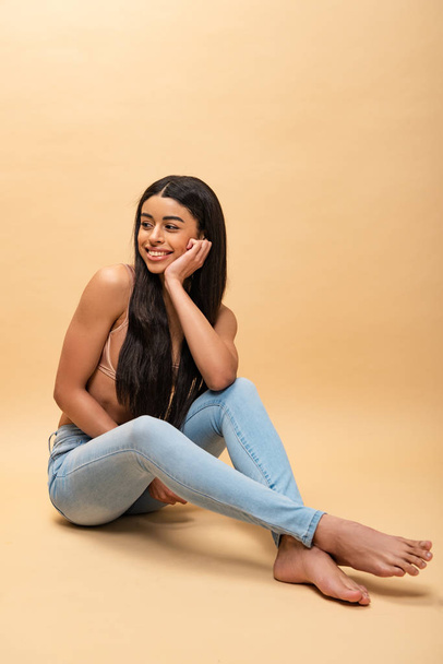 happy african american girl in blue jeans and bra sitting and looking away - Foto, Imagem